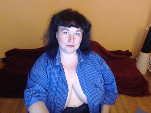 ErinSmart ha la pelle chiara, i capelli scuri e ondulati, e indossa una camicia blu a quadri aperta, che lascia scoperte le sue grandi tette chiare e nude. È seduta su un pavimento di legno..