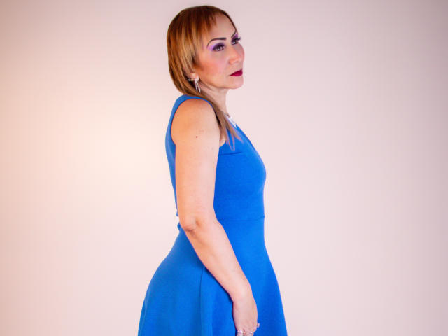 DianeOasis with blonde hair, wearing a blue dress, has a slim build, small tits, and a confident look, standing side profile, smiling with red lipstick.