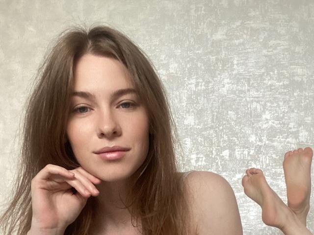 MineVicy ha lunghi capelli castani, pelle chiara e un leggero sorriso, con una mano sotto il mento e i piedi nudi sollevati in aria. Non si vedono vestiti..