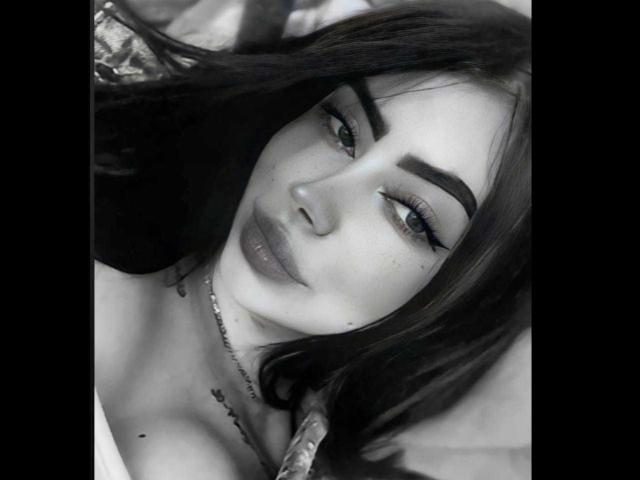 CristallEvans has dark, thick eyebrows, full lips with shiny lipstick, and long, wavy hair. She's lying down, looking at the camera with a slight, sexy smile.
