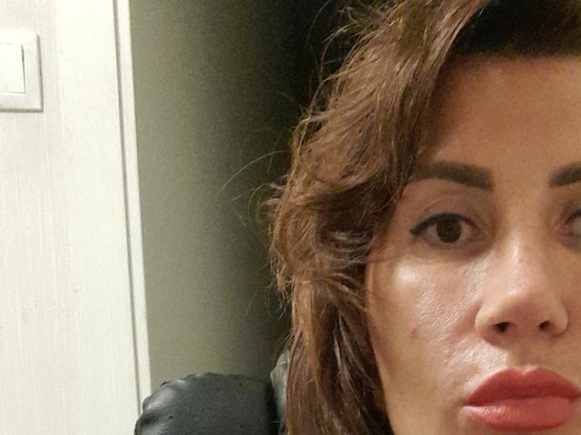 Il viso di RoxolanaSexy, con i capelli castano ondulati, le sopracciglia folte e un piccolo brufolo sulla guancia destra, con le labbra leggermente arricciate, in un selfie. Si vede il suo naso..