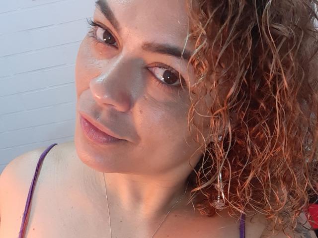 SolmaryHot ha i capelli castano ricci e umidi, la pelle chiara e un sorriso delicato. Indossa un reggiseno viola con spalline, da cui si intravedono piccoli seni rotondi, e una collana d'argento..