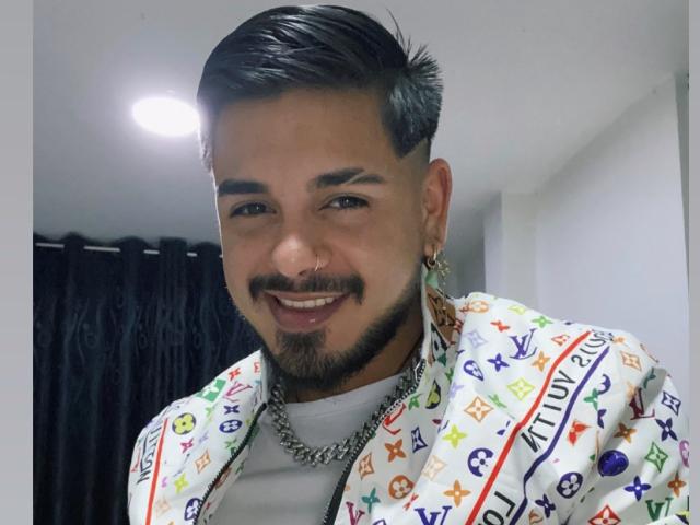 VisiI heeft een schattig, lachend gezicht met een donkere snor en baard, draagt een kleurrijke, gestreepte jas, een ketting en oorbellen, en heeft kort, glad achterover gekamd zwart haar..