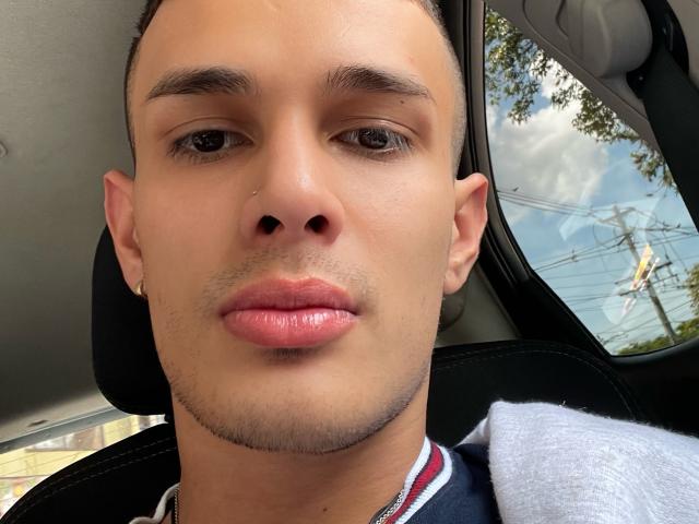SlimLewis has a light brown skin tone, short dark hair, small nose, and slightly glossy pink lips. He's wearing a tiny earring and has a slight goatee.