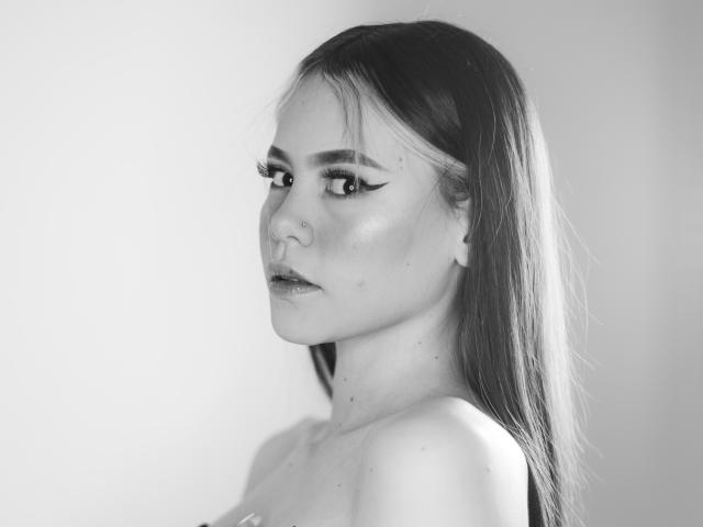 Jazmin Wells a de longs cheveux lisses, un anneau au nez et un trait d'eye-liner très marqué. Ses épaules dénudées et son expression sérieuse sont visibles dans un portrait en noir et blanc. Pas de seins visibles..