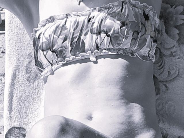 Xxandra's bare midriff with a ruffled, floral-patterned bandeau covering her tits. Her flat stomach and navel are visible. She's lying down on a textured towel.