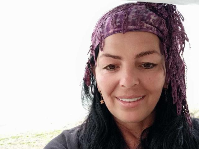 YulliaMilfX with purple knitted headwrap, black hair, brown eyes, smiling, wearing grey shirt, small gold earrings, looking cute.