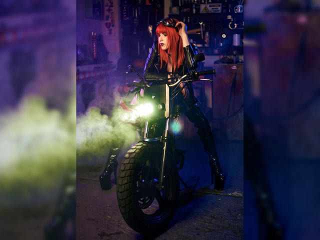 AliceRunner with red hair, black leather outfit, and high boots, riding a motorcycle with bright green smoke, in a dark, neon-lit urban setting. Her tits are visible.