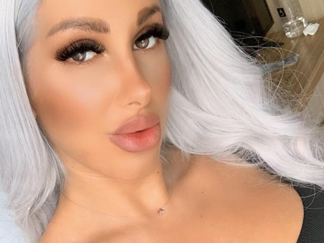 TanyaMonroe has platinum blonde hair, full lips, and is staring with green eyes. She has long, thick, black eyelashes and a small diamond necklace. Boobs are partially visible.