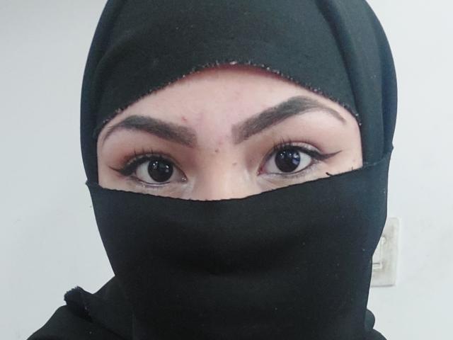 ElinaX's face with black hijab covering everything but her eyes, eyebrows, and a small part of her forehead. Her eyes are wide and brown with long eyelashes.