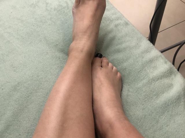 LadyMiller's legs crossed at the ankles, with her bare feet showing black-painted toes, resting on a green, fuzzy surface. Her skin is light brown.