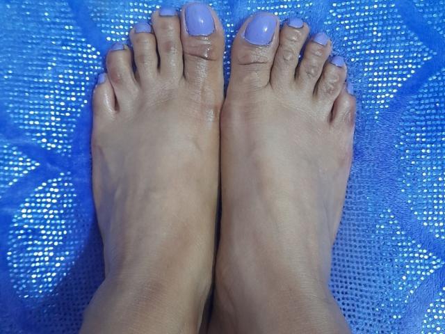 De voeten van RoxyLatin zijn geverfd met lichtpaarse nagellak, de tenen wijzen omhoog, de huid is licht glanzend, de tenen staan dicht bij elkaar, er ligt een blauwe, gestructureerde mat eronder..