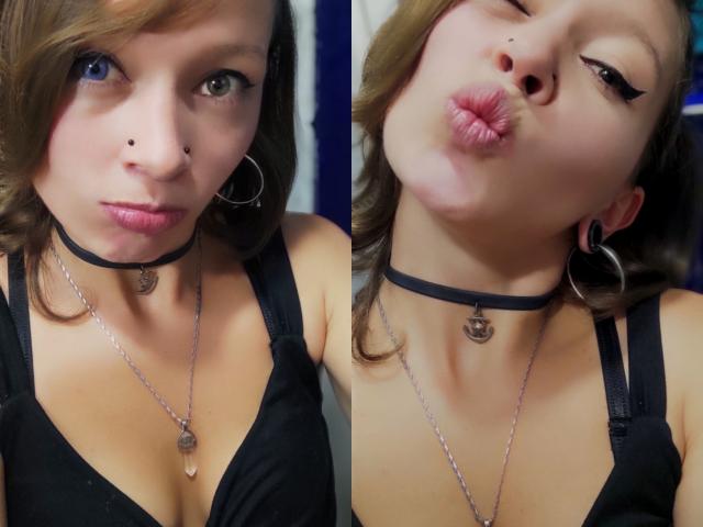 GoddessLufe tem pele clara, cabelo castanho, delineador preto, colar preto, um pequeno piercing no nariz, sutiã preto e lábios carnudos em duas selfies lado a lado, mostrando seu peito e beijando seus lábios..