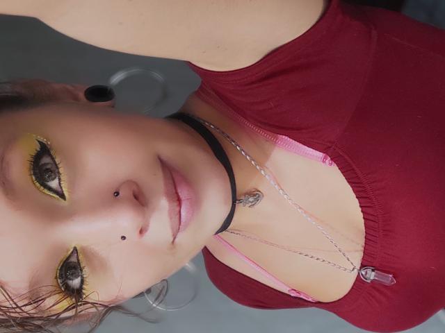 GoddessLufe avec du fard à paupières jaune, des élargisseurs d'oreilles noirs, des piercings au nez, un collier noir, un soutien-gorge rose, un haut rouge et un collier, montrant son visage et sa poitrine dans un autoportrait..