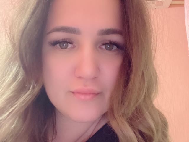 AnnabelleAllie has a cute face with green eyes, long wavy brown hair, and subtle makeup. She's looking directly at the camera with a slight, confident smile.