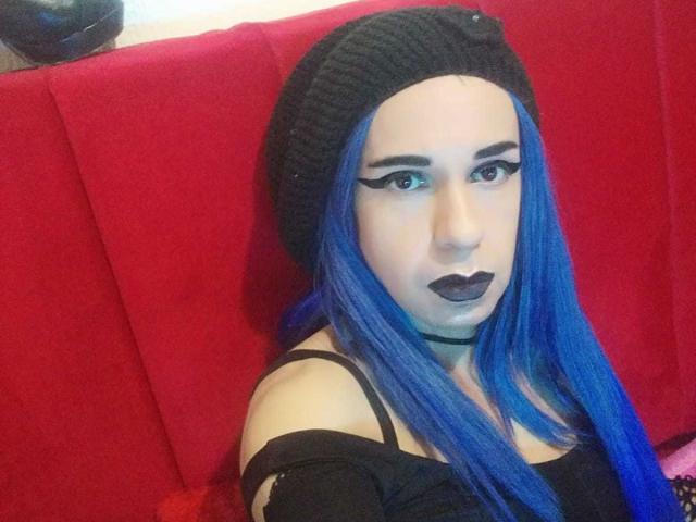 Bellanida with bright blue hair, black beanie, dark lipstick, and black off-shoulder top, sitting on red bench, showing her tits and cute face.