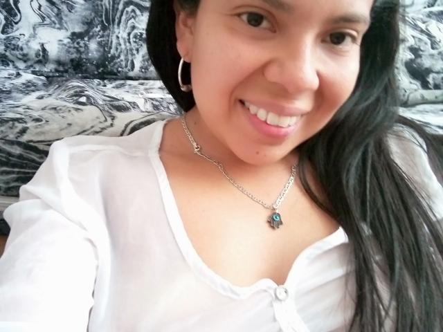 EstrellaBelle with long black hair, smiling, wearing a white button-up shirt, silver necklace with a blue gem, and hoop earrings, showing her cute nose and small tits.
