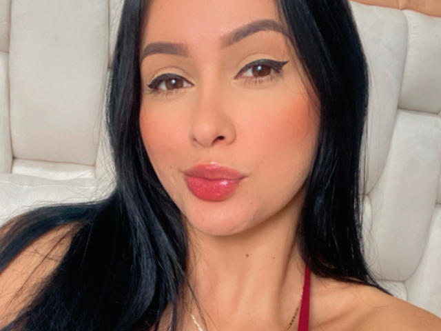 EmilyParkerr has pouty pink lips, black straight hair, brown eyes with winged eyeliner, and a cute tan complexion. Her red halter top is visible.