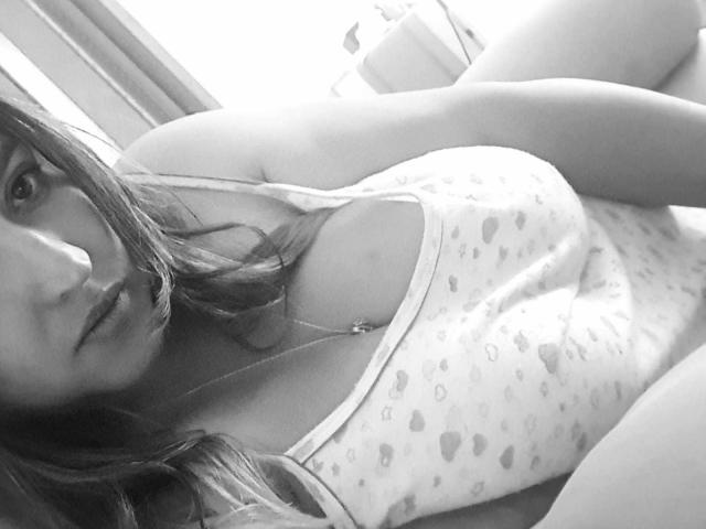 Fotografia in bianco e nero di NinaZorya con i capelli lunghi, che indossa una canottiera con spalline sottili e motivo a cuori, che mostra il seno, sdraiata, che guarda la fotocamera, con un sorriso appena accennato..