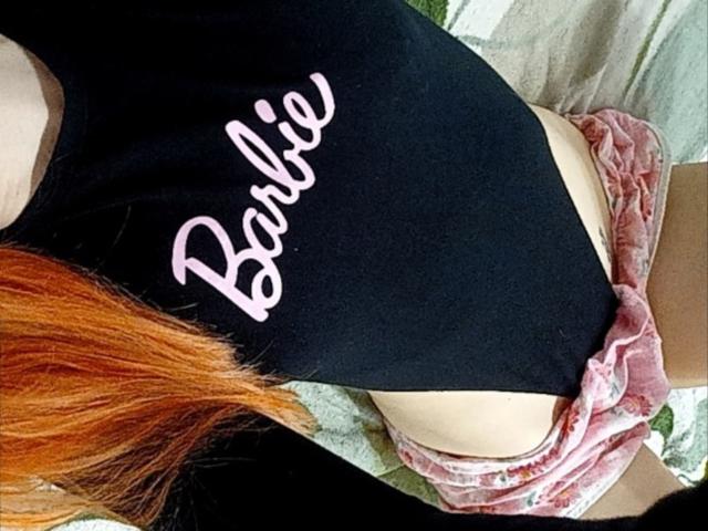 La maglietta nera di SweetyPieX con la scritta "Barbie" in lettere rosa, i pantaloncini di velluto rosa e i capelli rossi. Il suo sedere è visibile sopra i pantaloncini. Scatto dall'alto..