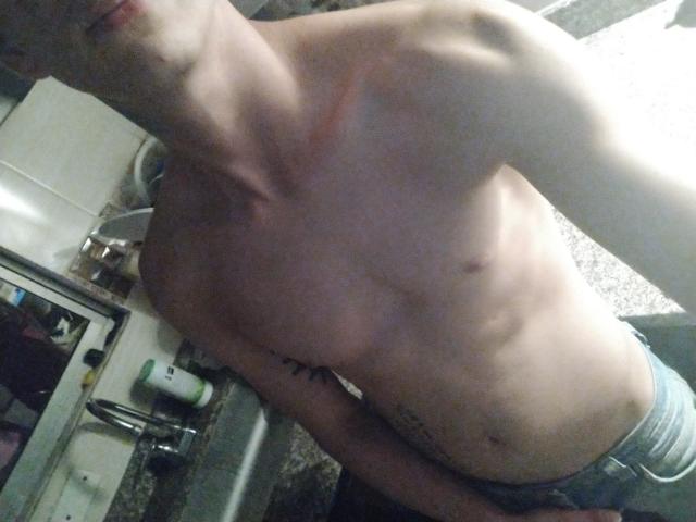 LatinAndres est torse nu, avec une silhouette mince et musclée, et une cage thoracique visible, et porte un jean bleu. Il/Elle a un petit tatouage sur le côté droit et une marque rouge sur la poitrine..