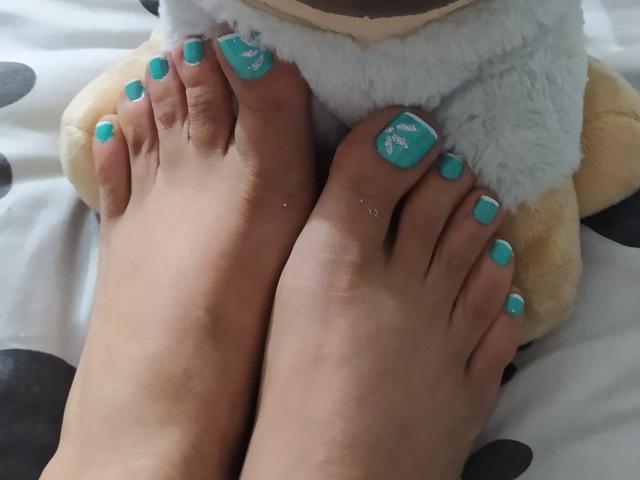DalilaSuperHot's feet, showing her bare toes with bright turquoise nail polish, resting on a stuffed animal. Her toes are slightly dirty, with a small sparkle on the big toe.