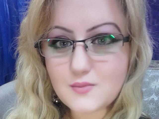 SeductiveBodyX with blonde hair, green-tinted glasses, and pink lips, looking directly at the camera, has a subtle smile and light makeup.