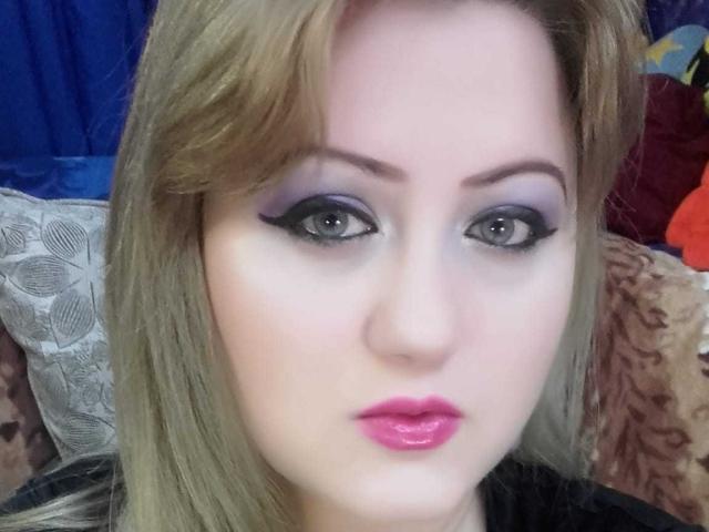 SeductiveBodyX has blonde hair, blue eyeshadow, black eyeliner, pink lipstick, and pale skin, staring directly into the camera with a slightly pouty expression.