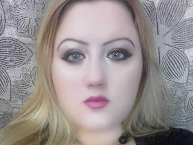 SeductiveBodyX has pale skin, blonde hair, dark eyeliner, and pink lipstick. She's looking straight at the camera with a neutral expression. Boobs not visible. Ass not visible. Pussy not visible.
