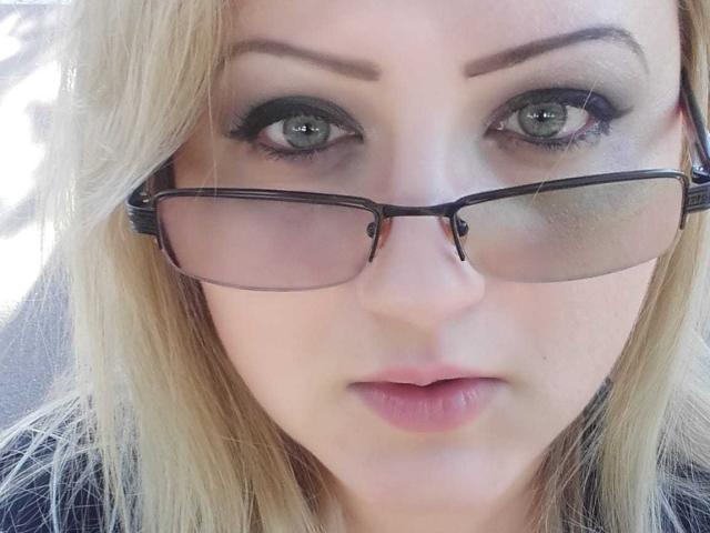 SeductiveBodyX with green eyes, black-framed glasses, and blonde hair, has slightly parted pink lips, looking directly at the camera with a neutral expression.