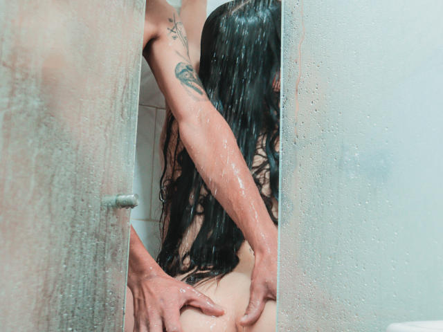 Il sedere bagnato di TeddyAndHottie viene toccato dalle mani del partner di TeddyAndHottie sotto la doccia, con l'acqua che gocciola, i lunghi capelli neri di TeddyAndHottie che coprono la schiena, e un tatuaggio visibile su TeddyAndHottie..