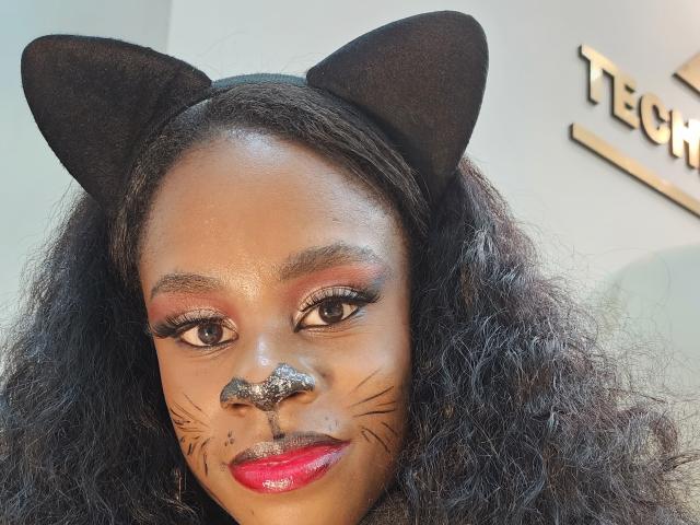 MiaHopson with cat ears, glitter nose, black whisker makeup, red lipstick, and curly black hair. She's looking at the camera with a serious expression.