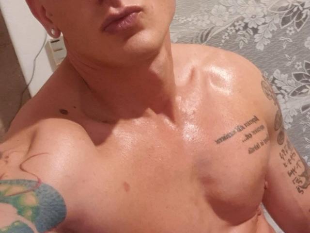 TonyLove69's shiny, muscular chest with tattoos, showing a tattooed right arm and a tattoo on the left side. No clothes, visible upper body, slightly parted lips.