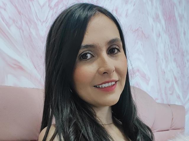 AmbeerBlack ha lunghi capelli neri, occhi marroni e un sorriso carino. Indossa un rossetto rosa e una collana, ed è seduta su una sedia in pelle rosa..