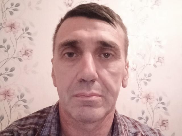Mr. Kentos, mit ernstem Gesicht, kurzen braunen Haaren, leichten Falten und einem karierten Hemd, das Nase und Lippen zeigt. Seine Augen sind braun und er blickt direkt in die Kamera..