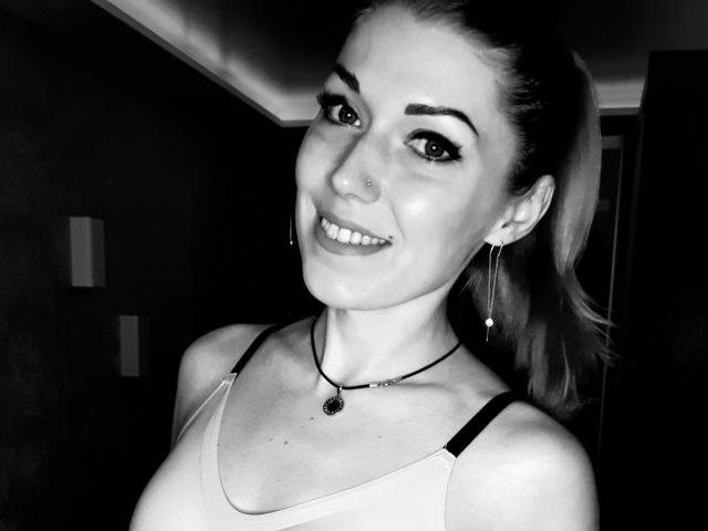 NikiSport hat ein Lächeln mit dunklem Eyeliner, einen Nasenring, Ohrringe, eine Halskette und einen Pferdeschwanz, trägt ein Tanktop, das ihre Brüste zeigt, und hat ein süßes Gesicht..