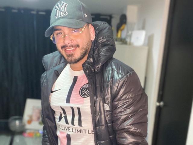 Uomo con carnagione media, barba e occhiali, che indossa un giubbotto imbottito nero, un cappellino dei New York Yankees e una maglietta sportiva bianca con dettagli rosa e neri. Sorride e guarda verso la telecamera..