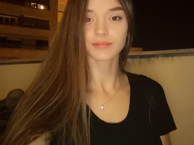 SonyaLovelace, con lunghi capelli castani, indossa una maglietta nera e una piccola collana con un ciondolo a forma di cuore, ha un sorriso appena accennato e una pelle chiara, in una stanza poco illuminata..