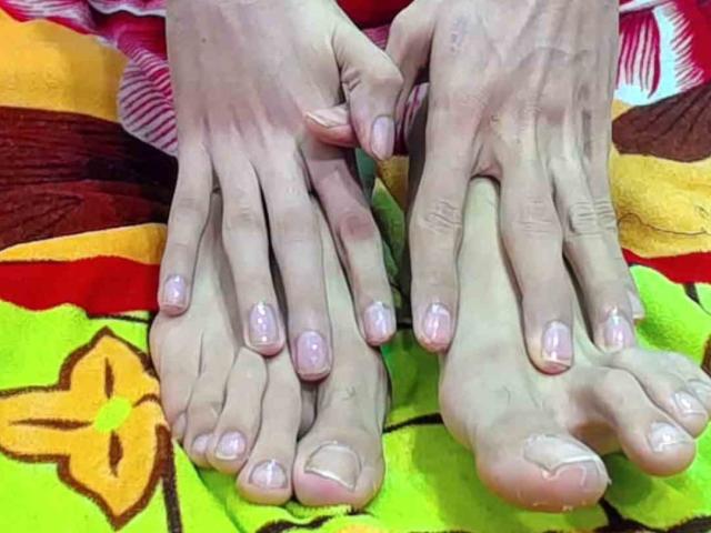 Die nackten Füße von HornyGay69, mit rosa Nagellack, die Zehen leicht gekrümmt, ruhen auf einem bunten Handtuch. Die Hände halten die Füße sanft, die Finger sind leicht gespreizt. Die Füße sind sauber, die Zehen sind ordentlich geschnitten..