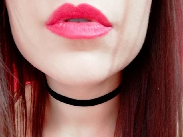Los labios rosados y brillantes de SugarrSanndy ocupan el centro del encuadre, con un collar negro alrededor de su cuello y el cabello castaño rojizo cayendo a ambos lados..