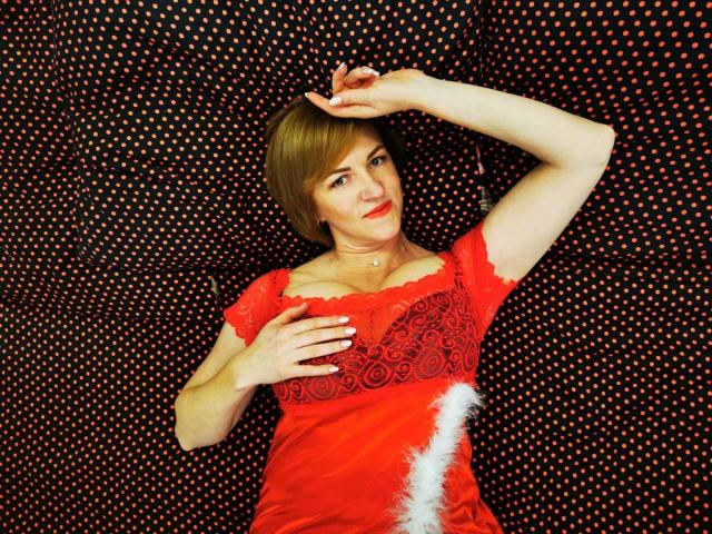 FeliziaStar with short brown hair, red lace dress, and white fur accent, lying down, hand on head, hand on tits, smiling, black polka dot background.