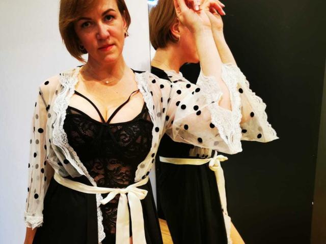 FelisiaStar with short brown hair, wearing a black lace bra with strappy details, black polka dot sheer robe, and white belt, standing in front of a mirror.