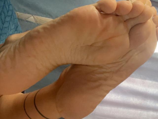 Misstyk's sole is in focus, showing wrinkled, slightly dirty toes with a black anklet, positioned with the heel up. Her foot is tan and the photo is tight.