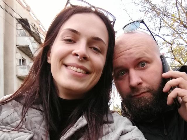 CuteReadyCpl has a cute smile, nose ring, and dark hair. Bald CuteReadyCpl with a beard, holding a phone, looks goofy. Both wear jackets, standing outside.