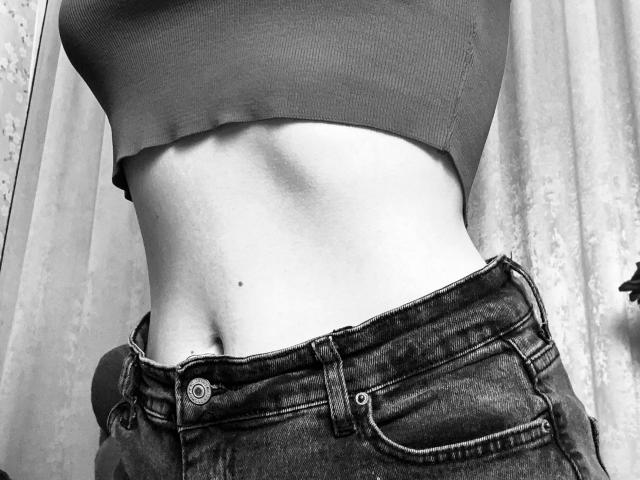 KarKutie's midriff with a small mole, wearing a crop top and dark denim jeans, buttoned but slightly unzipped. Black-and-white image.
