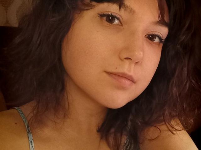 Carrie, avec ses cheveux noirs bouclés, ses yeux marrons et une petite beauté sur sa joue gauche, portant un bandeau bleu, regardant légèrement vers la droite avec une expression neutre..
