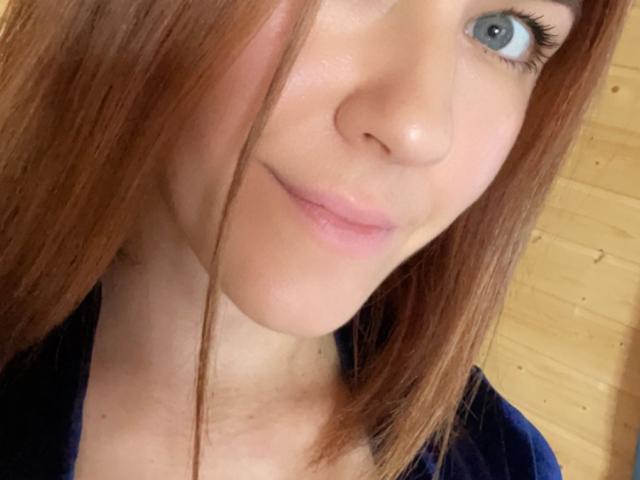 Misstyks Gesicht zeigt blaue Augen, hellrosa Lippen und glattes, braunes Haar mit einem leichten Seitenzopf. Sie trägt ein dunkelblaues Hemd. Ihre Nase ist klein und ihre Haut ist hell..