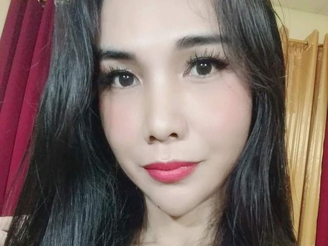 MissHotAyaLove has long black hair, dark eyes, thick eyelashes, pink lipstick, and a cute smile. Her skin is pale, and she looks sexy with a slight blush.