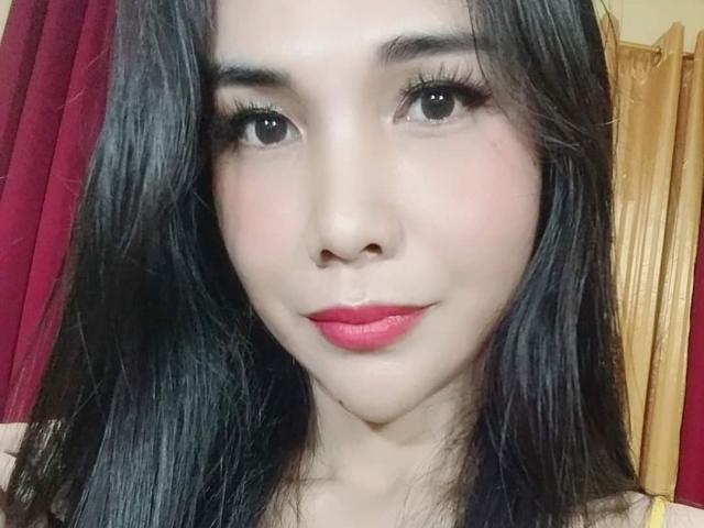 MissHotAyaLove con capelli neri lucidi, occhi scuri, rossetto rosa e un sorriso carino, che mostra il suo viso delicato e la sua pelle liscia. Il seno non è visibile, solo un primo piano del suo viso sexy..