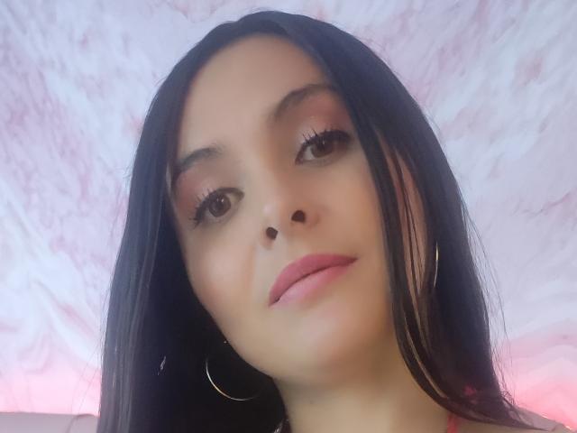 AmbeerBlack a de longs cheveux noirs, des yeux marrons, du fard à paupières rose, du rouge à lèvres rose, et des boucles d'oreilles cerceaux, avec un léger sourire et un teint clair et doux..